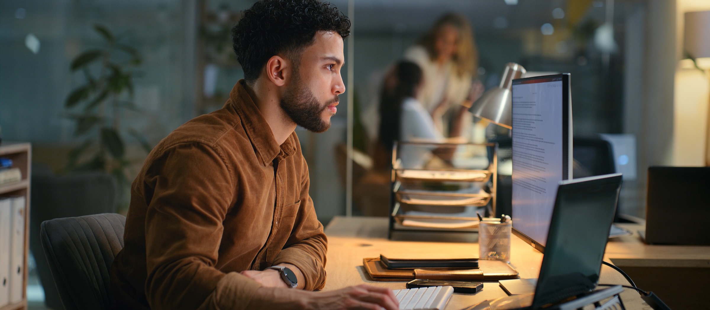 A focused professional working at a desk in a warmly lit office at night.